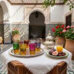 Silver tea set with multicolor glasses and fresh figs on a white table in a sunlit Moroccan courtyard
