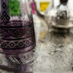Close-up of purple beldi glass with black arabesque pattern on an engraved tray from a silver tea set