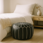 Black leather floor ottoman with geometric white stitching used as bedroom footrest beside modern bed