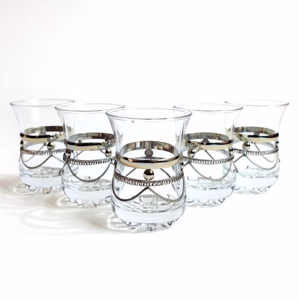 Studio lineup of six clear moroccan tea glasses with ornate silver chain bands, displayed against a white background.