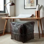 Dark brown square leather floor ottoman under wooden desk in home office with natural lighting