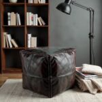 Square leather floor ottoman with cream stitching in industrial loft setting near exposed brick wall