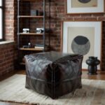 Square leather floor ottoman positioned at white vanity desk in minimalist bedroom with round mirror