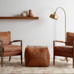 Light brown square leather ottoman between armchairs in modern living room, versatile handmade pouf for seating