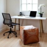 Light brown square leather ottoman under desk in home office, compact handmade pouf for extra seating