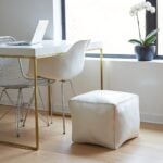 Modern white square leather pouf ottoman beside contemporary desk and chair in minimalist workspace