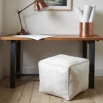 White square leather pouf under wooden desk with copper lamp for home office footrest seating