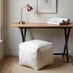 White square leather pouf ottoman tucked under white vanity desk in elegant bedroom setup