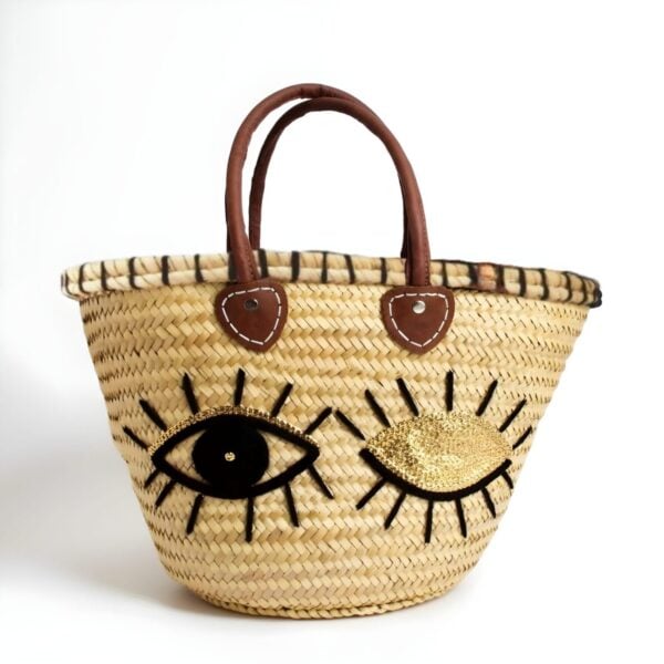Straw tote bag with winking eye sequin design and brown leather handles on white background