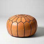 Studio view of a handcrafted tan leather round ottoman isolated on a white background.