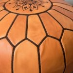 Macro close-up showing the embroidery and stitching details on the top of a leather round ottoman.