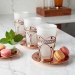 Two frosted white moroccan tea glasses in silver metal sleeves on white saucers with assorted macarons