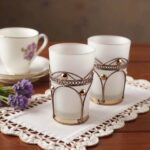 Frosted white moroccan tea glasses with silver-tone filigree holders on white lace cloth with lavender