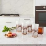 Six white moroccan tea glasses with silver filigree sleeves on marble surface with fresh mint and macarons