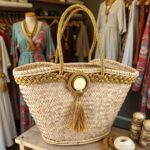 Gold straw bag on patio table, handwoven palm leaf tote with gold braided trim and tassel