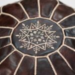 Close-up detail showing the intricate star-shaped stitching and contrasting thread on a dark brown leather round pouf.