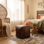A dark brown square leather ottoman placed on a patterned rug in a bohemian-style bedroom featuring a large wicker chair.
