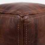 Close-up detail showing the handcrafted corner stitching and natural texture of a dark brown square leather ottoman.