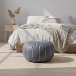 Gray leather round ottoman 21 inch pouf with white stitching placed beside minimalist bedroom