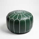 Studio photograph of a beautiful deep green leather floor ottoman with stark white hand-stitching.