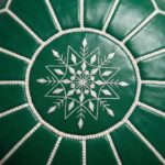 Top-down close-up of the intricate white silk embroidery and craftsmanship on a Moroccan green leather floor ottoman.