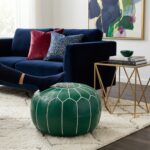 A modern blue sofa paired with a green leather floor ottoman being used as a comfortable footrest on a patterned area rug.