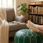 Cozy home office or reading corner featuring a green leather floor ottoman used as a footstool next to a grey armchair and wooden bookshelf.