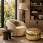 Gold leather round pouf paired with a boucle accent chair in a cozy reading nook featuring built-in shelving and natural daylight.