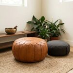 A zen meditation space featuring a leather round ottoman pouf next to a charcoal floor cushion and a singing bowl on a jute rug.