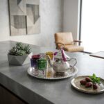 Modern kitchen styling of a silver moroccan tea set on a concrete countertop, featuring vibrant glasses and a signature magenta silk tassel.