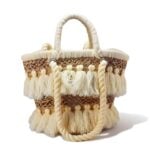 Handwoven beige tassel straw bag with cotton pom-pom fringe and wrapped rope handles on white background
