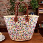 Handwoven Sequin Straw Bag against brick wall, multicolor confetti basket with brown leather straps