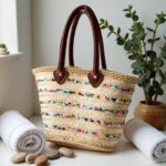 Colorful straw bag tilted open revealing lined interior and leather handle attachment with rivets on handwoven palm leaf body