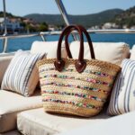 Colorful straw bag resting on boat cushions displaying multicolored sequin stripes and natural palm leaf herringbone weave