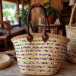 Colorful straw bag on rustic wood with multicolored sequin stripes pom pom trim and handwoven palm leaf herringbone weave