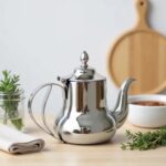 Polished stainless steel mirror finish teapot with domed lid and ergonomic handle on a kitchen counter
