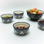 Black and white geometric ceramic serving bowls arranged on white shelving unit with cutting board
