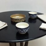 Hand-painted ceramic serving bowls with geometric black patterns on round black dining table