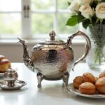 Ornate footed hammered silver teapot with hinged lid and dragon spout served with Moroccan pastries and tea glasses