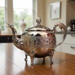 Close-up of royal engraved silver teapot large showing heraldic shields and geometric chiseled patterns