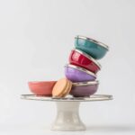 Tilted stack of ceramic bowls with silver trim on cake stand, displaying colorful artisan craftsmanship