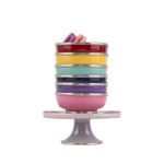 Stacked ceramic bowls with silver trim on pedestal, topped with purple and pink macarons