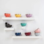Multiple ceramic bowls with silver trim arranged on white floating shelves, showing variety of colors