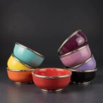 Stacked ceramic bowls with silver trim displaying red, yellow, turquoise, pink and purple colors on black