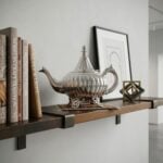 A decorative Ribbed Silver Teapot displayed on a wooden floating shelf next to design and craft books, accompanied by minimal modern decor in a bright room.
