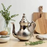 Minimalist hammered silver teapot featuring dimpled texture and curved handle on a polished wood table