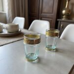 Two clear tea glasses with metal band and silver filigree sleeves on a wooden table in a dining room