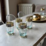 Group of clear tea glasses with metal band and ornate silver filigree sleeves arranged on a marble surface