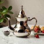 Mirror finish traditional moroccan silver teapot on marble with fresh strawberries and Moroccan tea glass