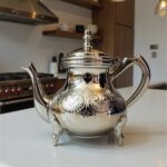 Silver-plated engraved teapot 6-cup with four ornate feet and curved spout in a kitchen